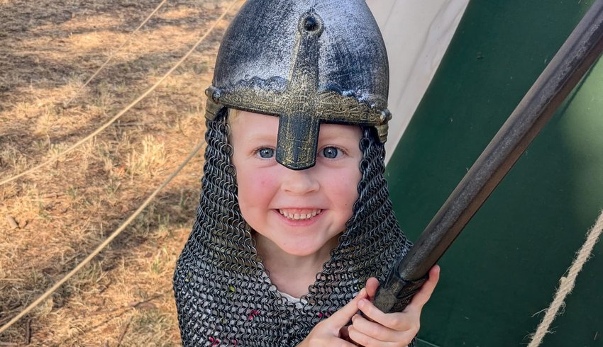 Eloise wearing a chainmail helmet and fake sword, smiling for a photo.