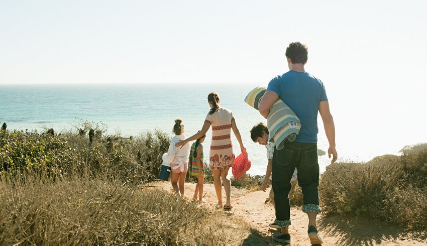 Family of five, carrying beach paraphernalia and walking to the beach.