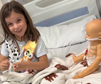Child in hospital receiving haemodialysis treatment and playing with dolls