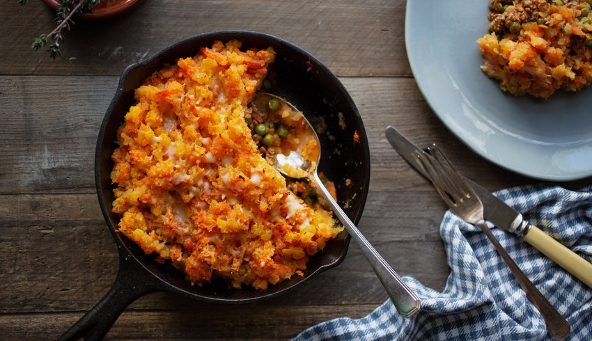 Sweet potato Shepherds Pie in a serving dish on a table with a plate and cutlery.