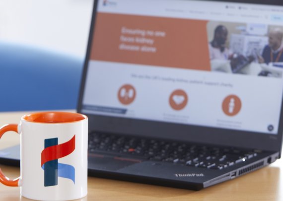 Kidney Care UK branded mug on a desk with a laptop. Open on the laptop is the Kidney Care UK website homepage.