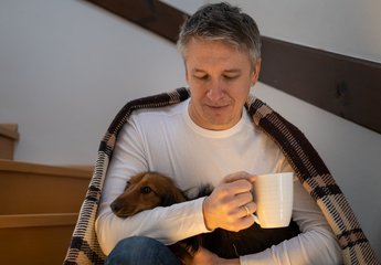 Man with dog and hot drink with blanket
