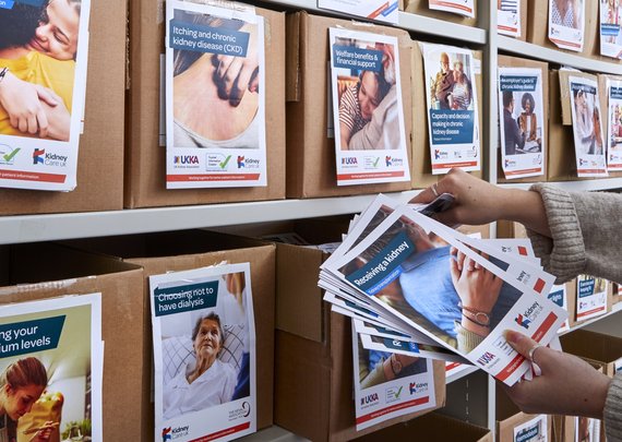 Person choosing Kidney Care UK patient information booklets from a wall of boxes full of different booklets.