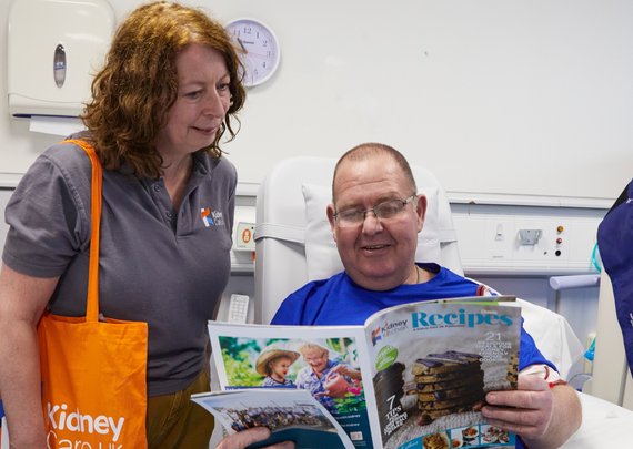 Kidney Care UK Patient Support & Advocacy officer, smiling with a patient who is receiving haemodialysis in a hospital unit. They are showing the patient a Kidney Kitchen magazine.