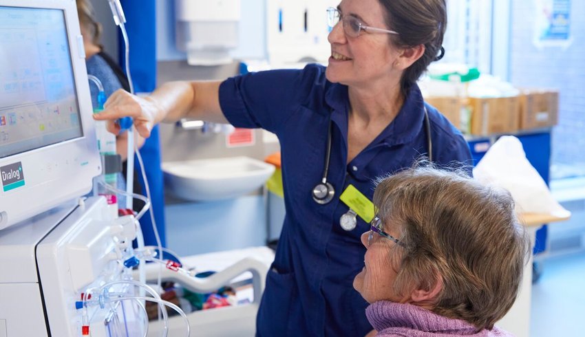 Nurse and patient looking at a dialysis machine screen together and smiling.