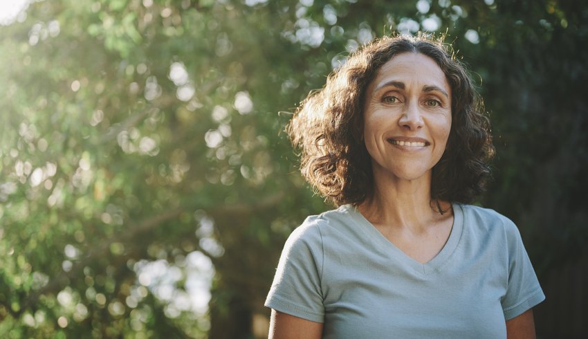 Woman walking outdoors in the sunshine wearing a short sleeved T-shirt and smiling.