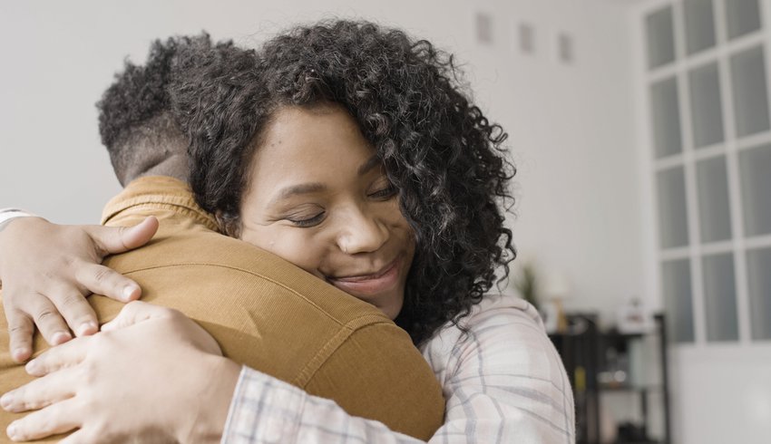 A woman hugging a man with her face shown and the man's back shown.