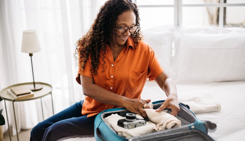 Woman packing clothes into a suitcase on a bed.